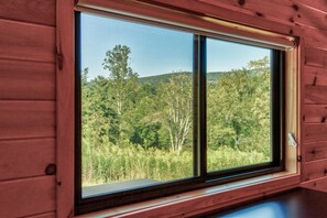 Ein Fenster mit Blick auf einen bewaldeten Hügel.