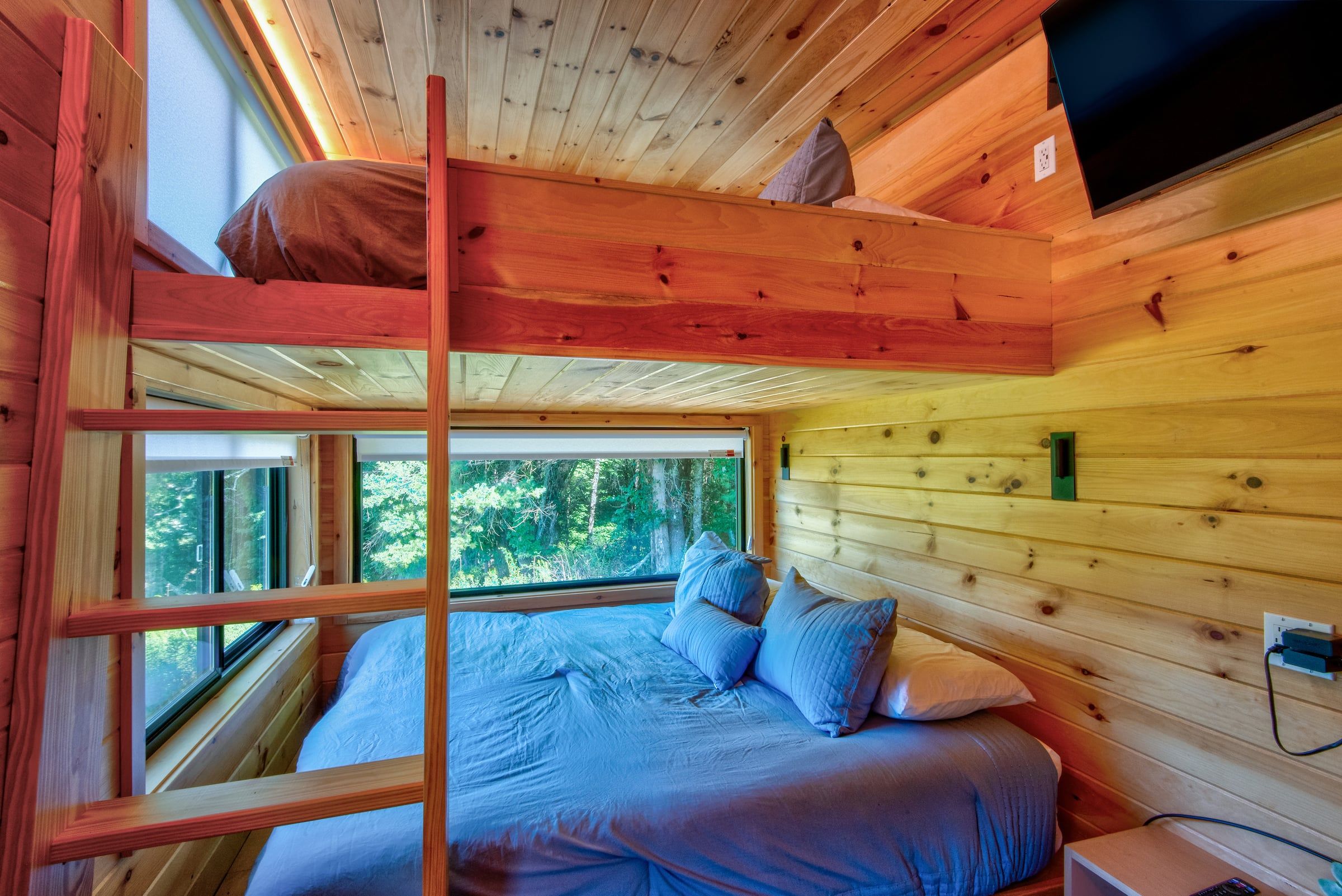 A bunk bed room with a window, a bed with pillows, and a television on the wall.
