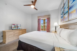 Ein Schlafzimmer mit einem Bett, einer Kommode, einem Deckenventilator, einem Fenster mit Vorhängen und Kunstwerken an der Wand.