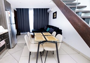 A modern living space with a dining table, chairs, a sofa, and a staircase. - Embassy Gardens Duplex by HDG (Accra)
