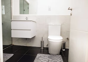 A bathroom with a toilet, a sink, and a mirror. - Embassy Gardens Duplex by HDG (Accra)
