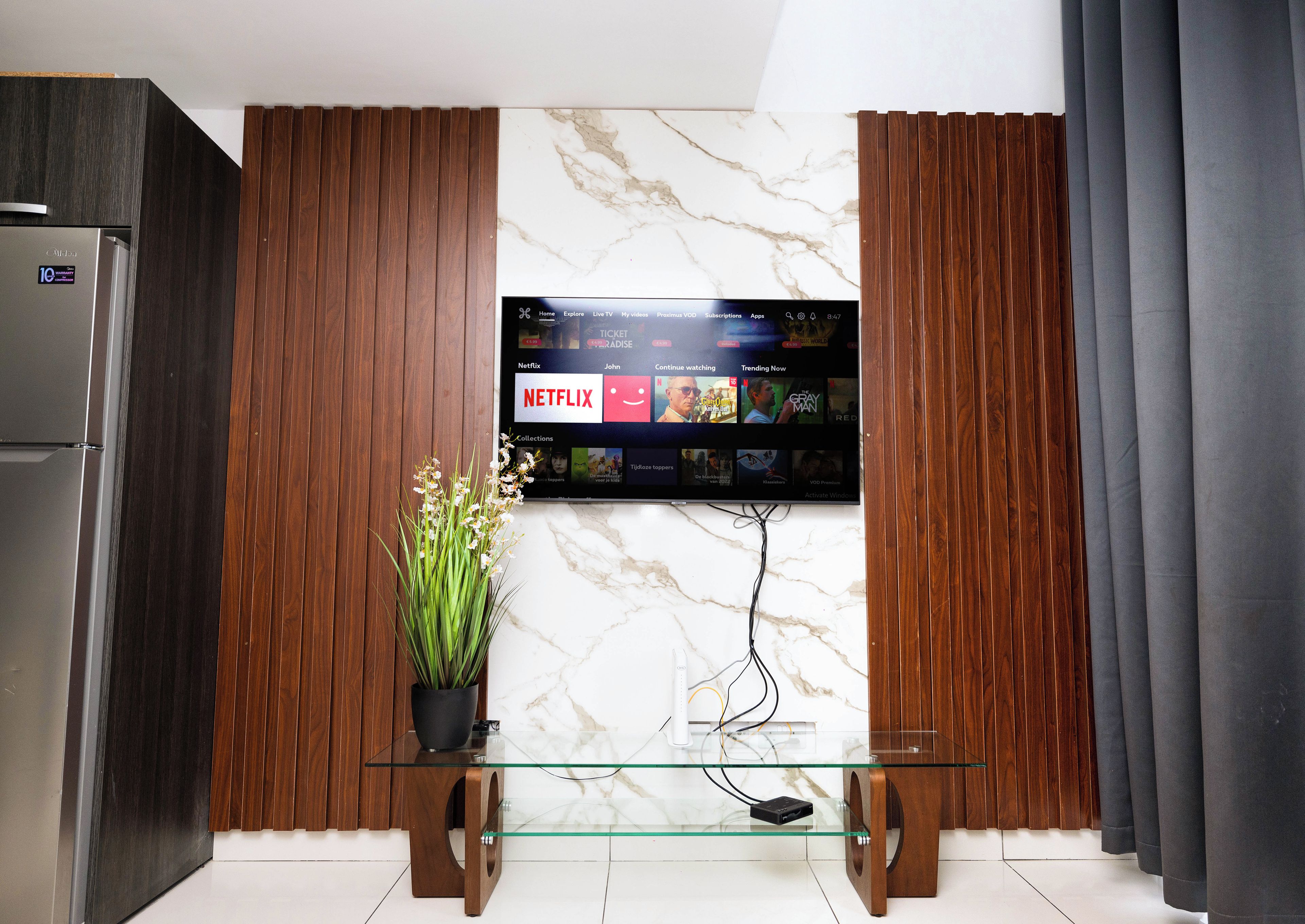 A modern living room with a flat-screen TV mounted on a wall, a glass coffee table, and wooden paneling.