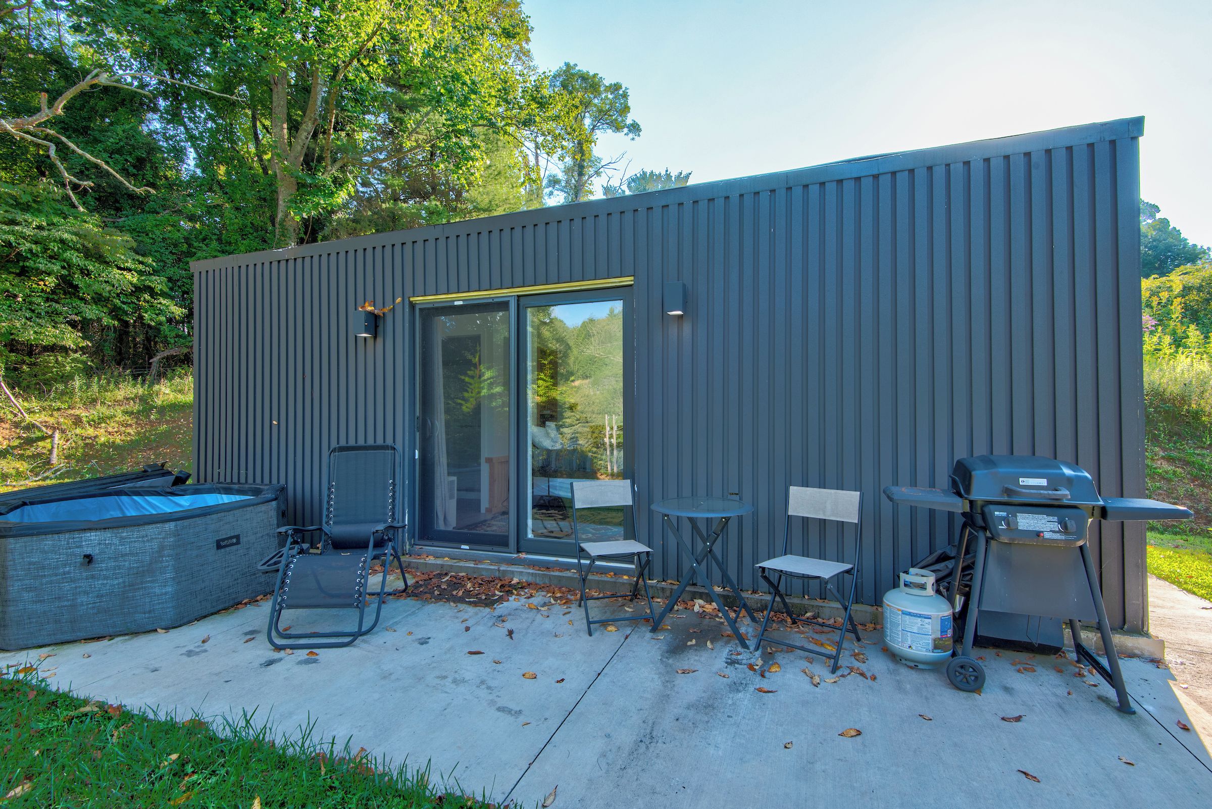 Een moderne buitenconstructie met een glazen deur, een zithoek en barbecuevoorzieningen.