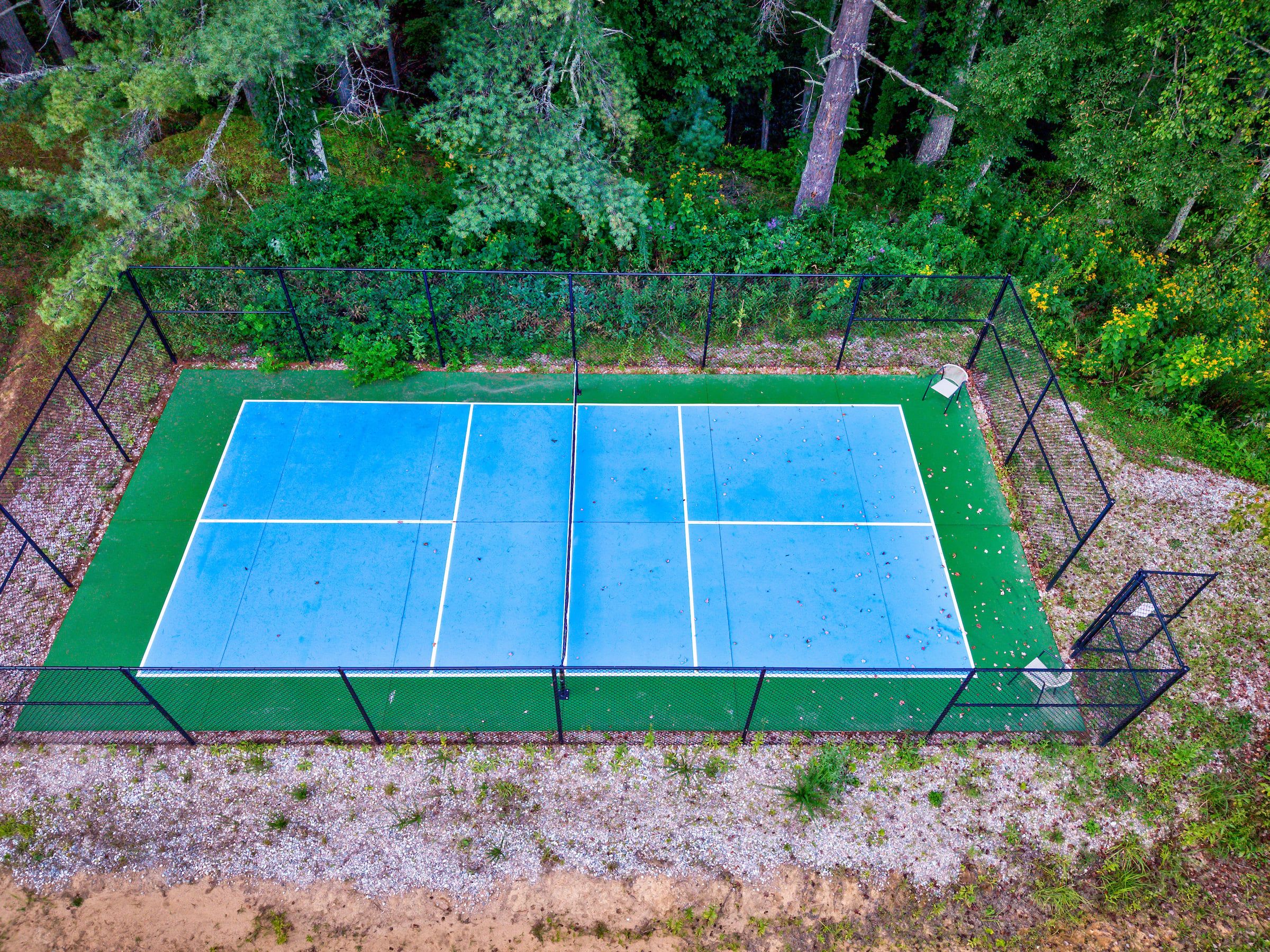 En udendørs tennisbane omgivet af tæt skov.