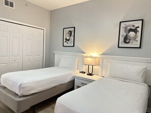 A hotel room with two beds, a nightstand with a lamp, and two framed pictures on the wall. - 1305 Stunning 3/3 Resort Condo Near Disney (Orlando)