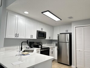 A modern kitchen with white cabinets, a stainless steel refrigerator, a microwave, and a coffee maker. - 1305 Stunning 3/3 Resort Condo Near Disney (Orlando)