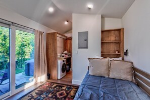 Ein Schlafzimmer mit einem Bett, einer Waschmaschine, einem Holzschrank und Blick auf Grünflächen.