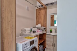 Ein Waschbereich mit Waschmaschine, Wäscheständer und Ablagefläche für Handtücher und Toilettenartikel.