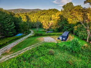 A rural landscape with a dirt path, a blue tennis court, and a small building with a dark roof. - Eagle Pod at Tiffany's Estate | Hot Tub, Fire Pit, Pickleball, & Pond (Elk Park)