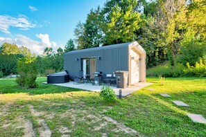 A compact outdoor structure with a patio area, seating, and a grill. - Eagle Pod at Tiffany's Estate | Hot Tub, Fire Pit, Pickleball, & Pond (Elk Park)