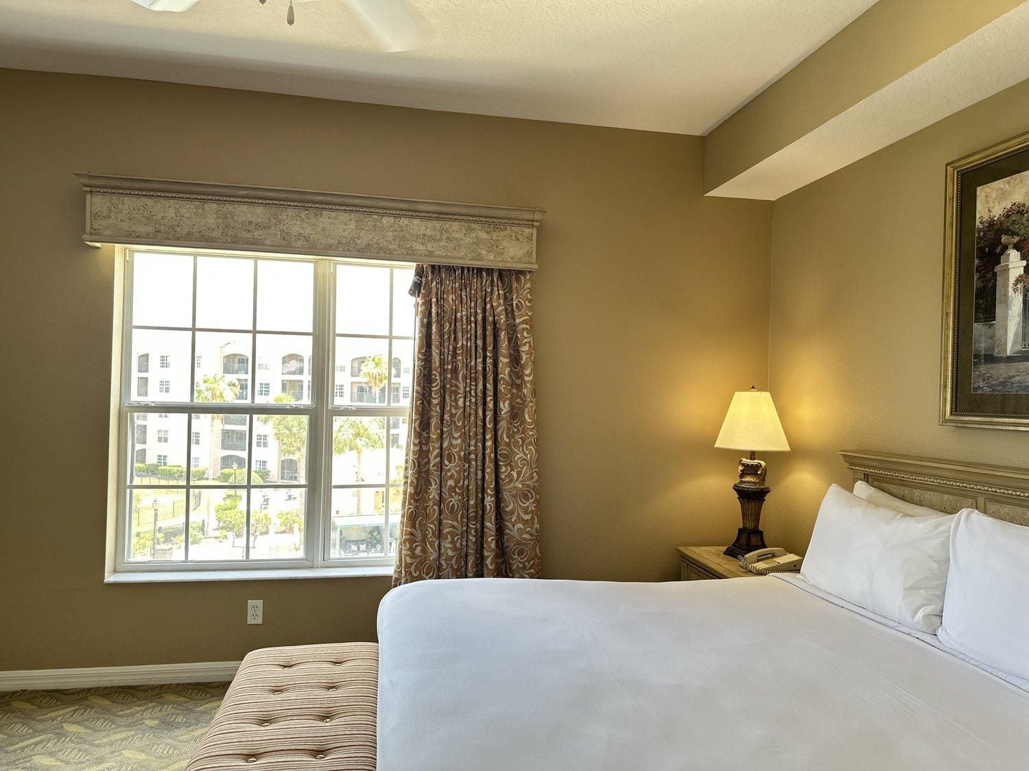 A hotel room with a large bed, a window with curtains, a bedside lamp, and a painting on the wall.
