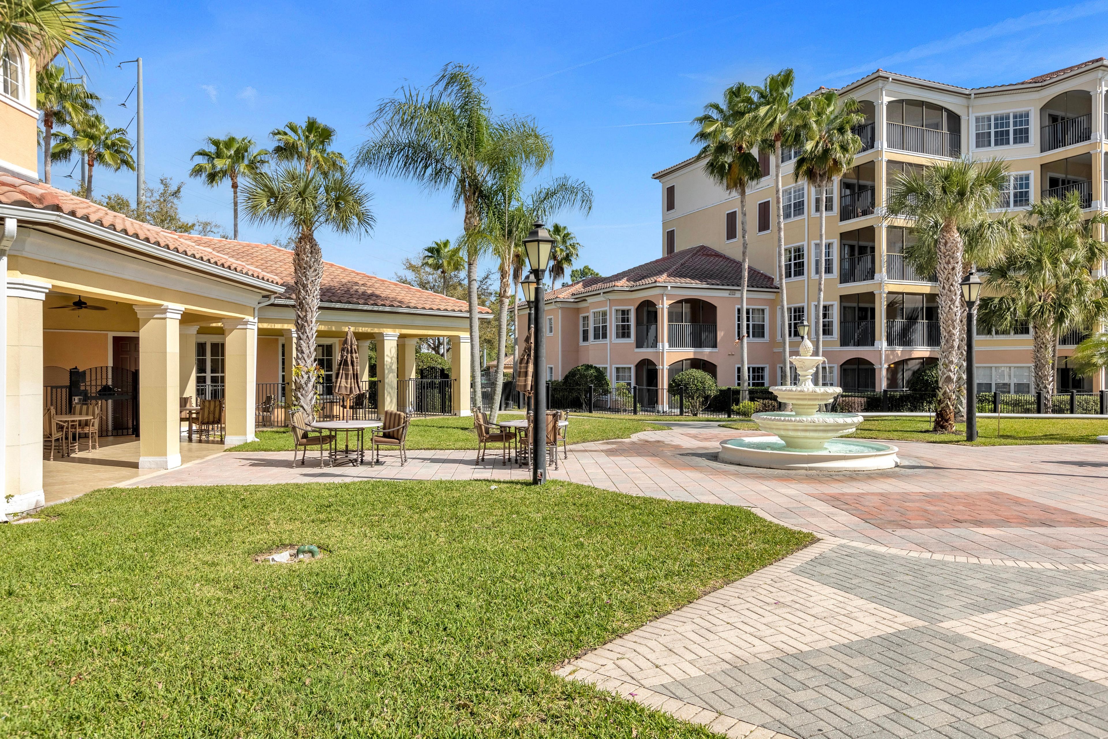 A courtyard with a fountain, palm trees, and a building with balconies.