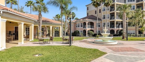 A courtyard with a fountain, palm trees, and a building with balconies.