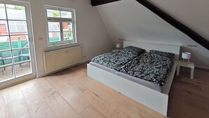 Quarto com teto inclinado, cama com roupa de cama estampada, radiador e janela com vista para prédios.