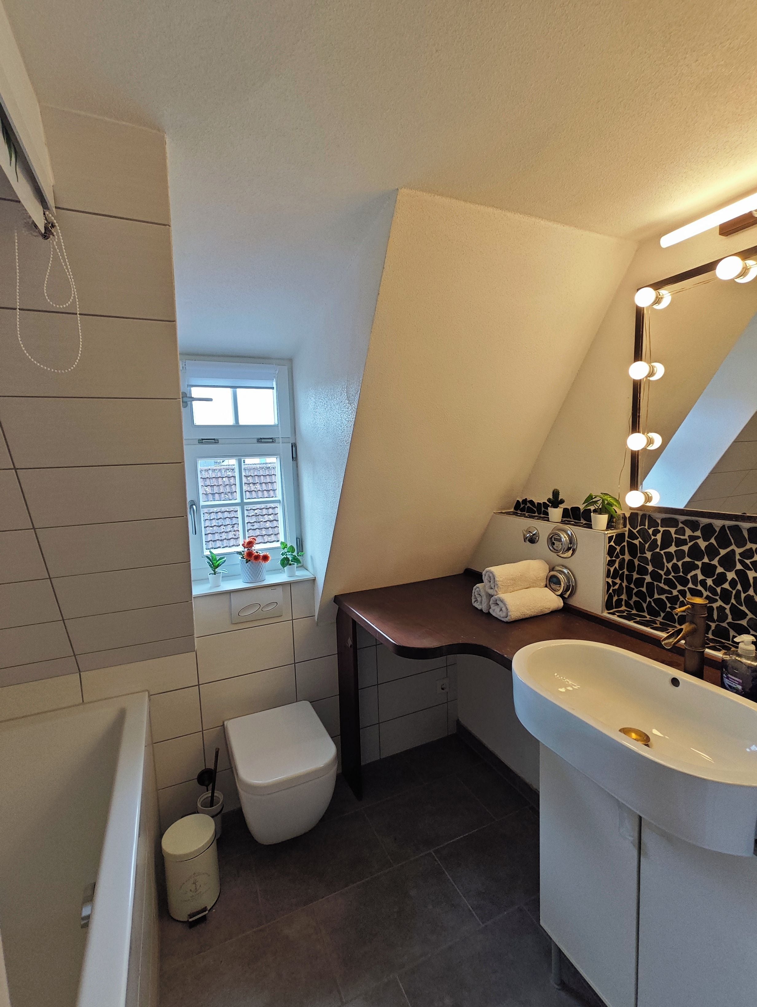 A modern bathroom with a large window, a vanity with a mirror, and a bathtub.
