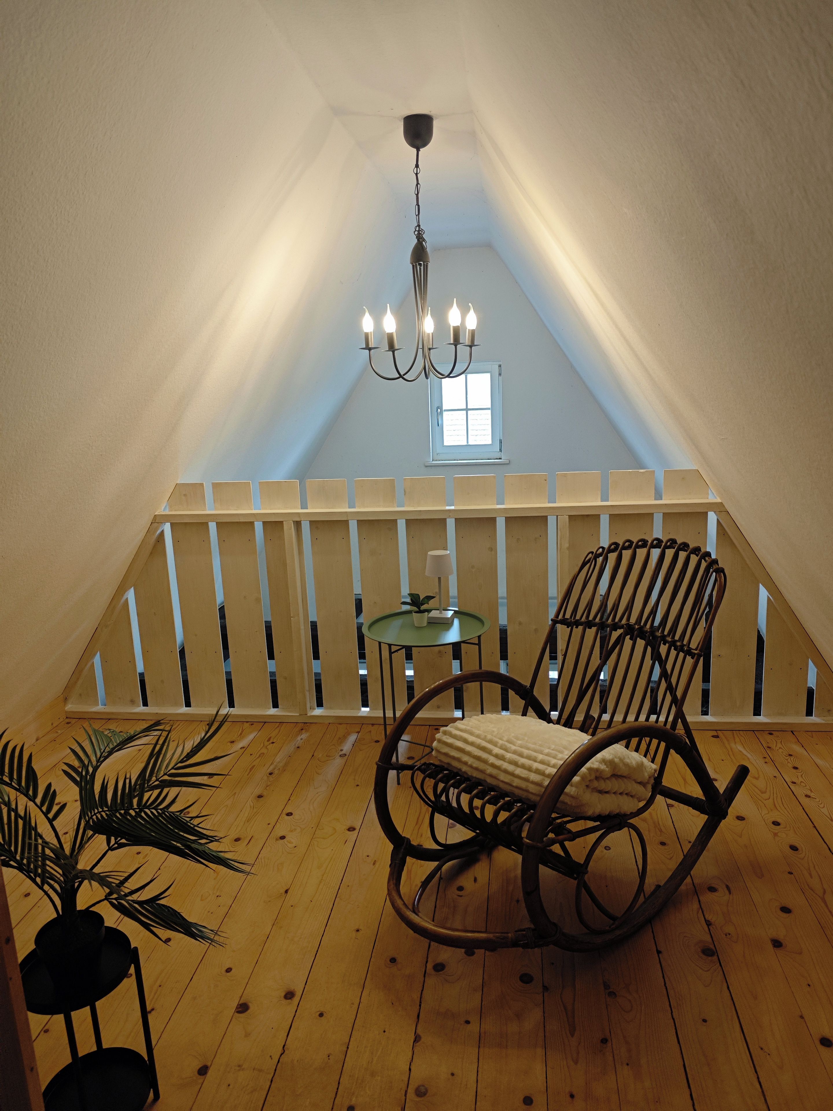 Ein Holzboden, ein Schaukelstuhl, ein kleiner Tisch mit einer Lampe und ein Fenster.