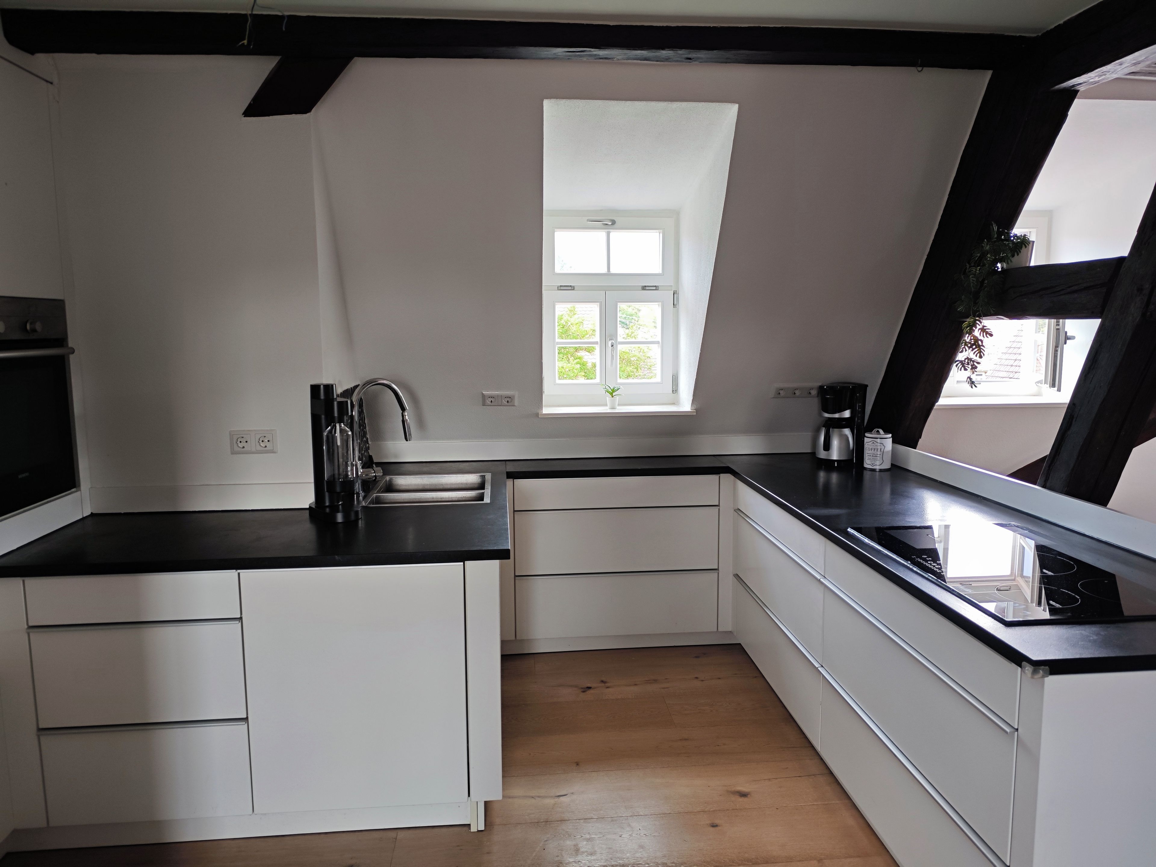 A modern kitchen with white cabinetry, a black countertop, a built-in oven, and a window with a view of greenery.