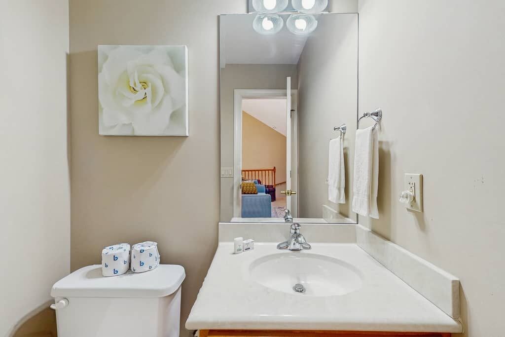 Une salle de bain équipée de toilettes, d’un lavabo et d’un miroir qui reflète une pièce comprenant un lit et une porte.