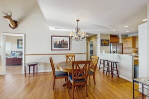 Un comedor con una mesa y sillas de madera, una araña y una cabeza de venado montada.