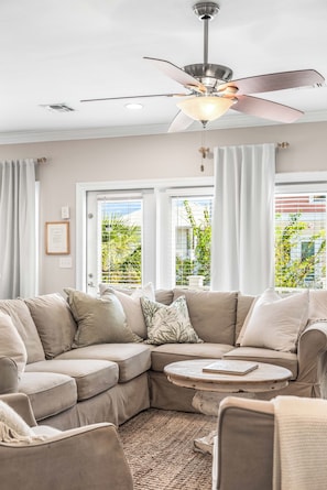 A modern living room with a sectional sofa, a round coffee table, and a ceiling fan. - Designer-Private Heated Pool-Golf Cart (Miramar Beach)