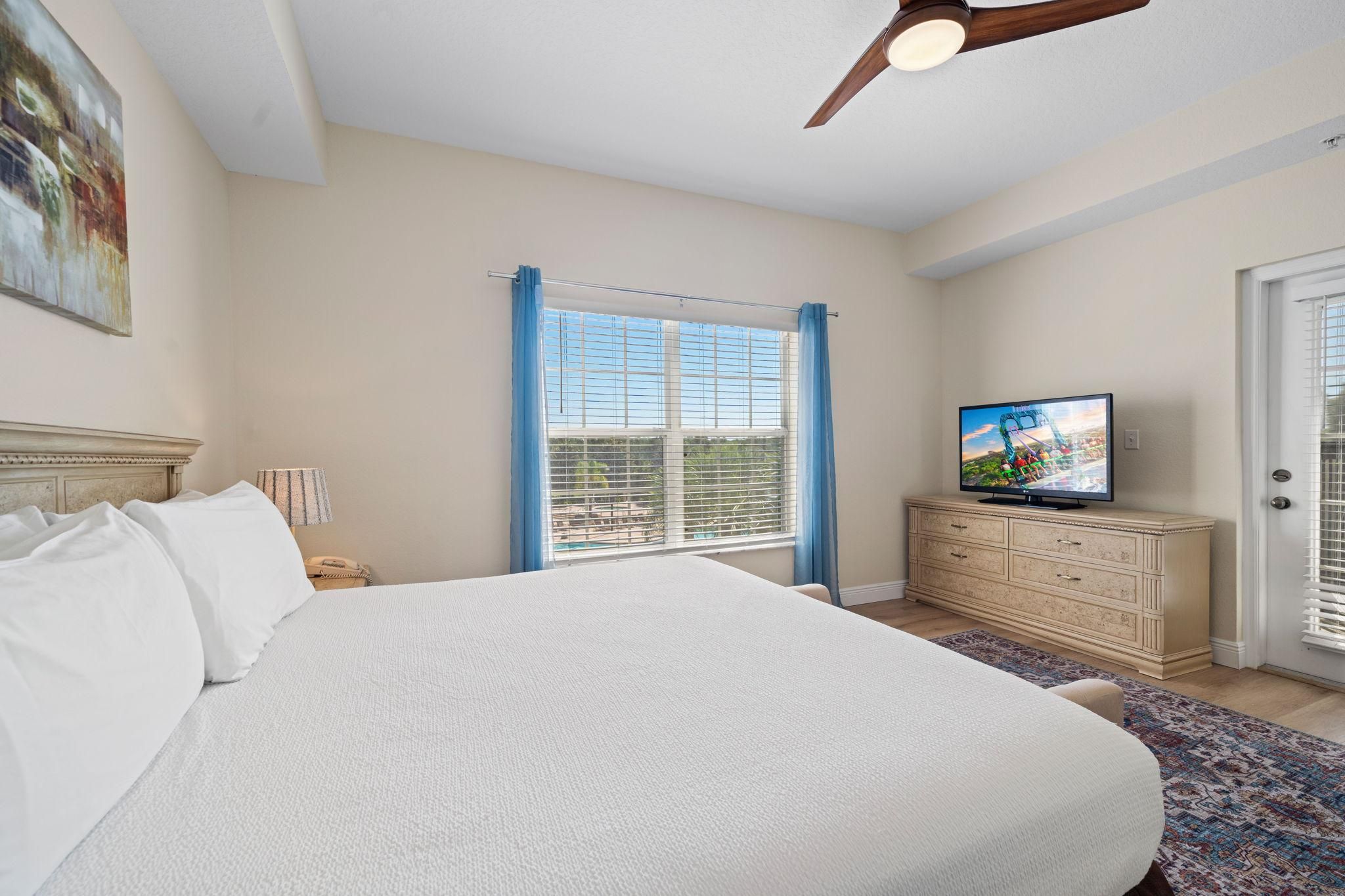 A bedroom with a large bed, a television, a dresser, and a window with blinds.