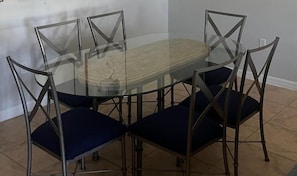 A round glass table with a wooden center, surrounded by four chairs with metal frames and dark cushions. - 2305 Spacious 3/3 Resort Condo Near Disney (Orlando)