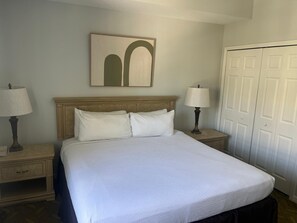 A hotel room with a bed, two bedside tables with lamps, a wall-mounted artwork, and a set of double doors. - 2305 Spacious 3/3 Resort Condo Near Disney (Orlando)