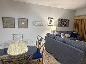 A living room with a grey sofa, a glass dining table with chairs, and framed artwork on the walls. - 2305 Spacious 3/3 Resort Condo Near Disney (Orlando)