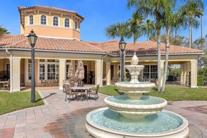 A courtyard with a fountain, outdoor seating, and a building with a tiled roof. - 2404 3B/3 Home Away From Home Near Disney (Orlando)
