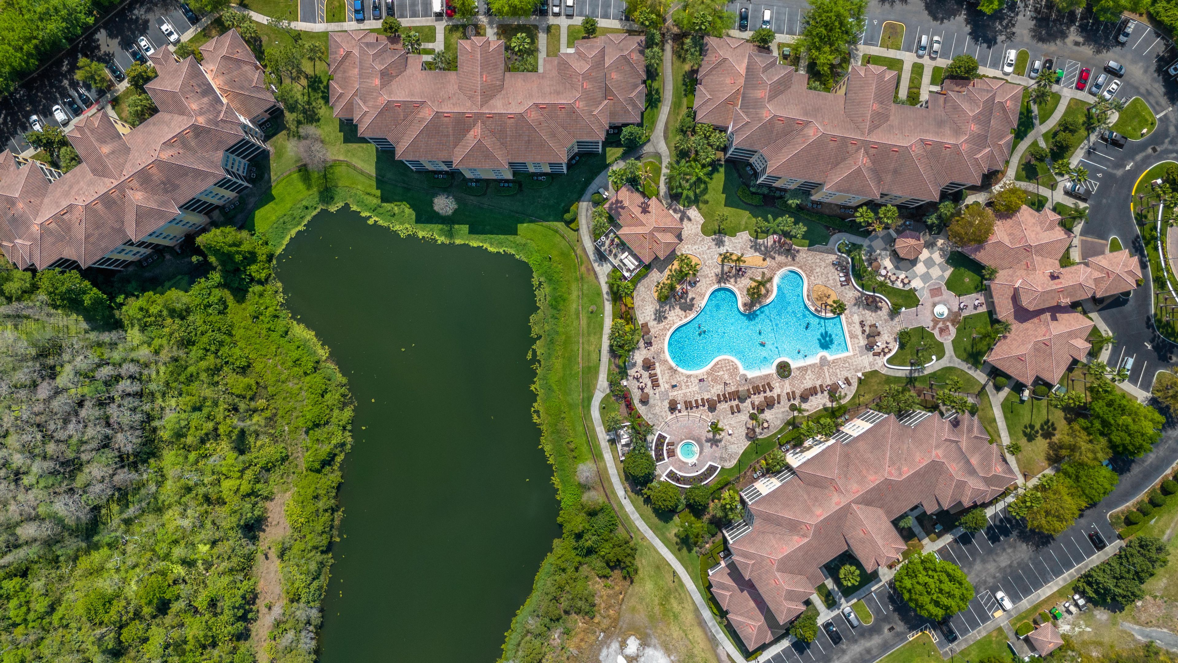 An aerial view of a residential area with multiple houses, a swimming pool, and a body of water.