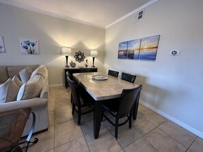 A dining area with a table and chairs, a sofa, and wall art. - 2404 3B/3 Home Away From Home Near Disney (Orlando)