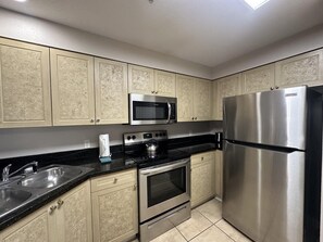 A kitchen with beige cabinetry, stainless steel appliances including a refrigerator, microwave, and oven, and a black countertop. - 2405 Spacious 3/3 Resort Condo Near Disney (Orlando)