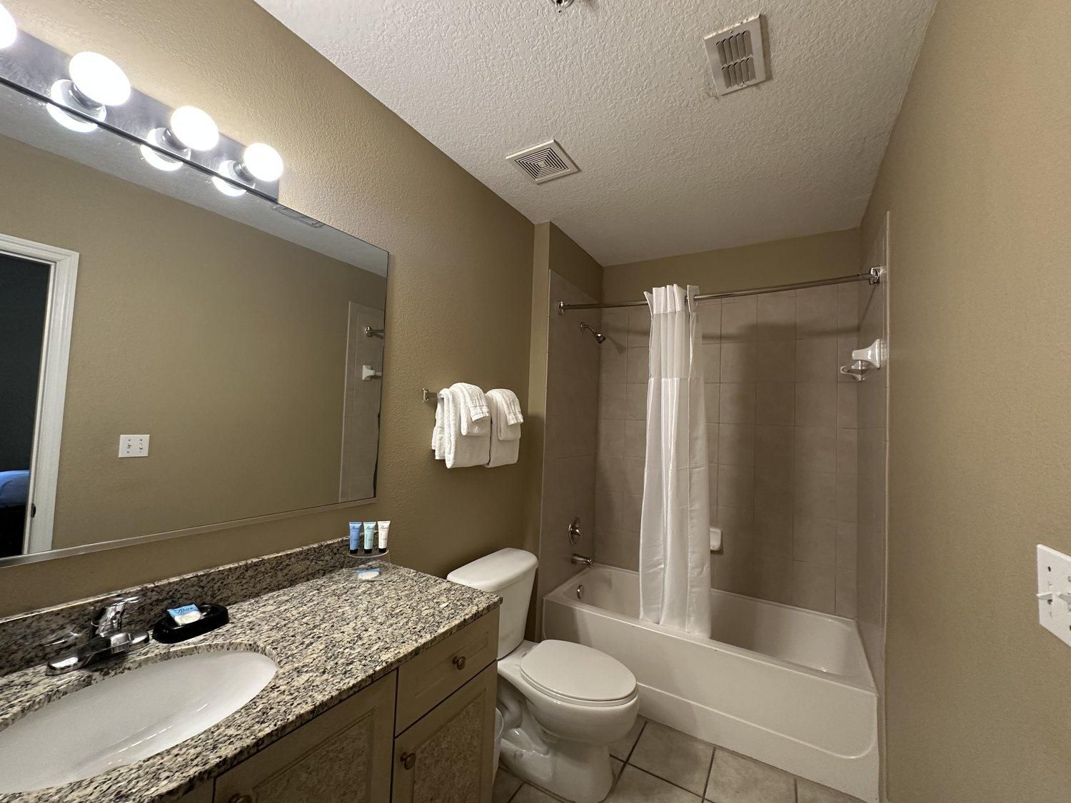 Une salle de bain avec un lavabo sur un plan de travail en granit, des toilettes, une baignoire et un rideau de douche.