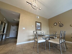 A dining area with a table and chairs, a ceiling light fixture, and a framed picture on the wall. - 2505 Spacious 3/3 Resort Condo Near Disney (Orlando)
