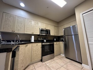 A kitchen with beige cabinetry, a stainless steel refrigerator, a microwave, and a stove. - 2505 Spacious 3/3 Resort Condo Near Disney (Orlando)