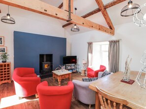 A living room with a fireplace, red chairs, a television, and a wooden table. - Hen Blas (Pwllheli)