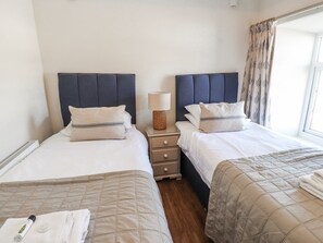 A hotel room with two beds, a bedside table with a lamp, and a window with curtains. - Hen Blas (Pwllheli)