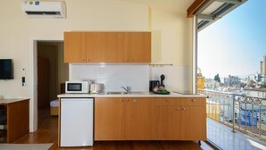 Una cocina compacta con armarios de madera, un microondas y un lavamanos. Hay un refrigerador pequeño y una ventana con vista a la ciudad.