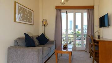 A living room with a grey sofa, a wooden coffee table, a TV on the wall, and a balcony with a view of the city.
