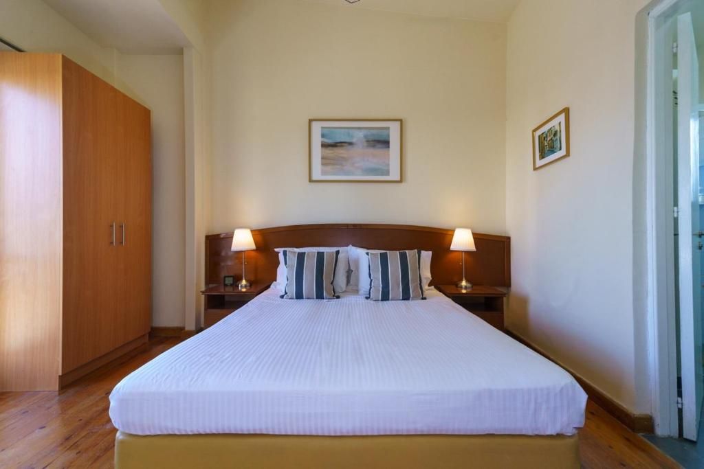 Una cama bien hecha con almohadas a rayas, un armario de madera y dos l ámparas de noche.