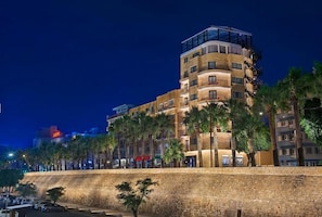 Un hotel de varios pisos con balcones, palmeras y un muro de contención de piedra.
