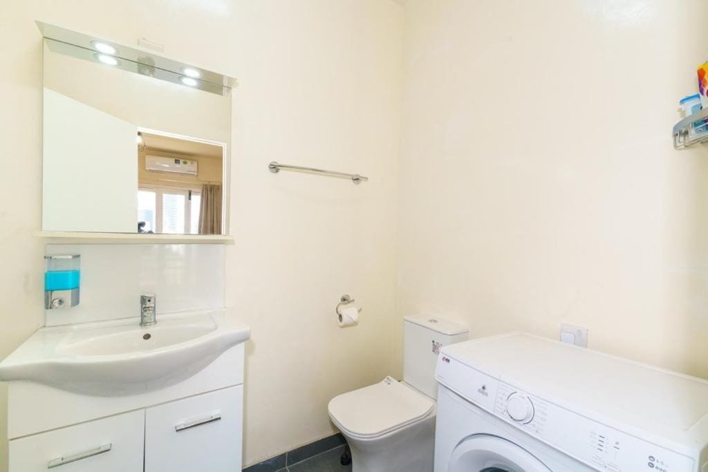 A small, clean bathroom with a sink, mirror, toilet, and a washing machine.