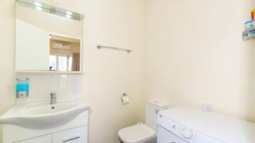 A small, clean bathroom with a sink, mirror, toilet, and a washing machine.