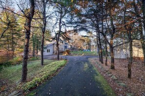 Zona residencial amb una calçada pavimentada que condueix a una casa envoltada d'arbres.