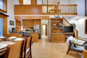 Une cuisine spacieuse avec des meubles en bois, un coin repas avec une table dressée pour quatre personnes, et un salon avec un canapé et un téléviseur.