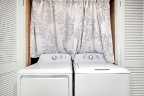 A laundry room with two stacked washers and dryers, a wooden door, and a white curtain with a leaf pattern. - 🌊 Lakefront Poconos Retreat | Private Beach • Kayaks • Fire Pits (Long Pond)