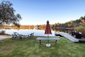 A lakeside outdoor seating area with a table, chairs, and an umbrella. - 🌊 Lakefront Poconos Retreat | Private Beach • Kayaks • Fire Pits (Long Pond)