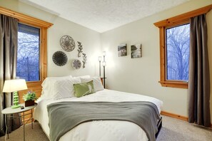 Une chambre à coucher avec un lit, une table de chevet avec une lampe et deux fenêtres avec des rideaux.