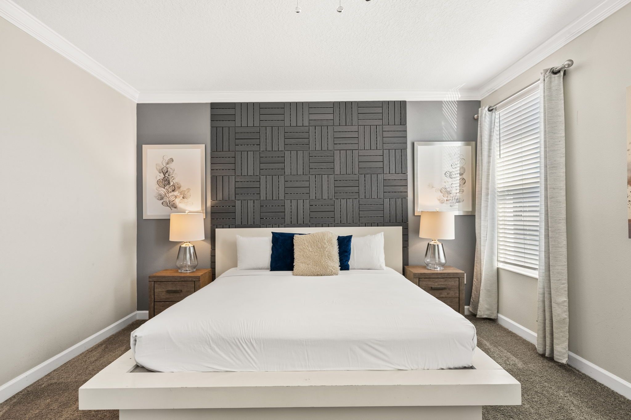 A bedroom with a bed, two nightstands, a wall-mounted headboard, and two framed artworks.