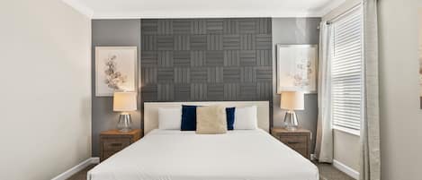 Quarto com cama, duas mesas de cabeceira, painel de cama fixado na parede e duas obras de arte emolduradas.